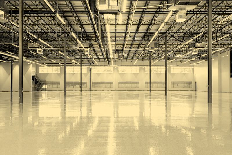 Empty warehouse space with a polished concrete floor, steel roof trusses and daylight along one wall